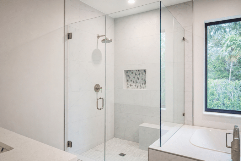 Modern bathroom with a glass-enclosed shower, built-in bench, niche with patterned tile, and a window showing greenery outside.
