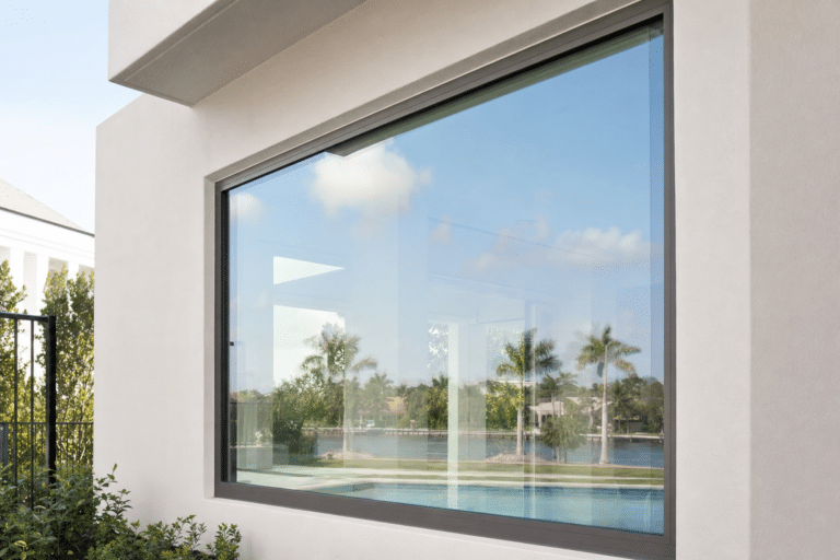 A large glass window reflects palm trees, water, and blue sky outside a modern white building.
